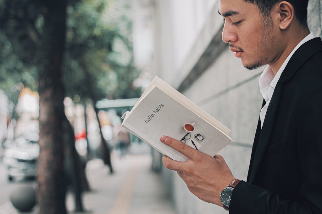 A man in a suit reading a book titled 'hello habits' on a city sidewalk.