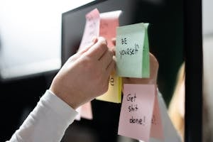 Close-up of hand placing colorful motivational sticky notes on a mirror, inspiring messages.