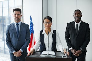 Diverse group of politicians in suits at a podium with American flag indoors.